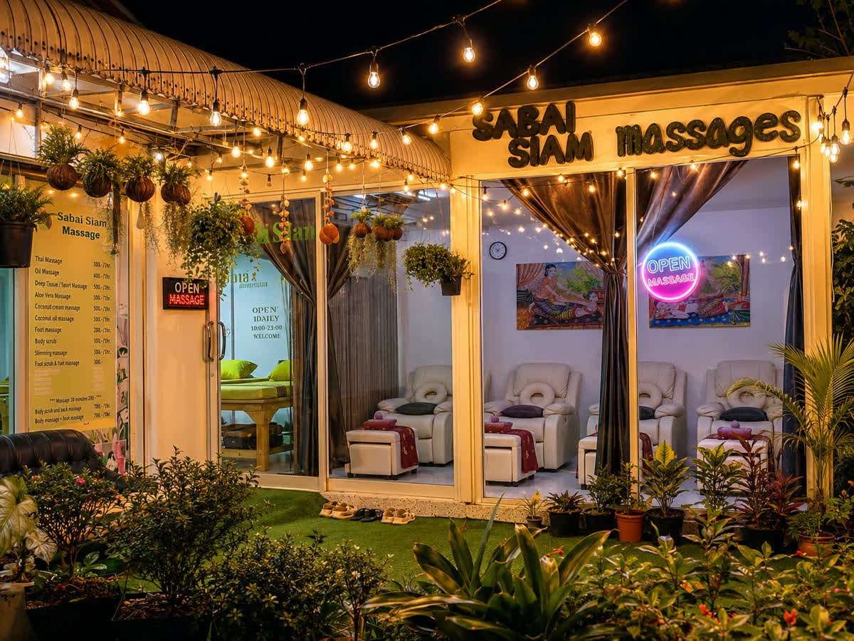 Sabai Siam seen from the road at night: the lit sign above the windows, string lights across the terrace, and the foot massage chairs visible through the glass.